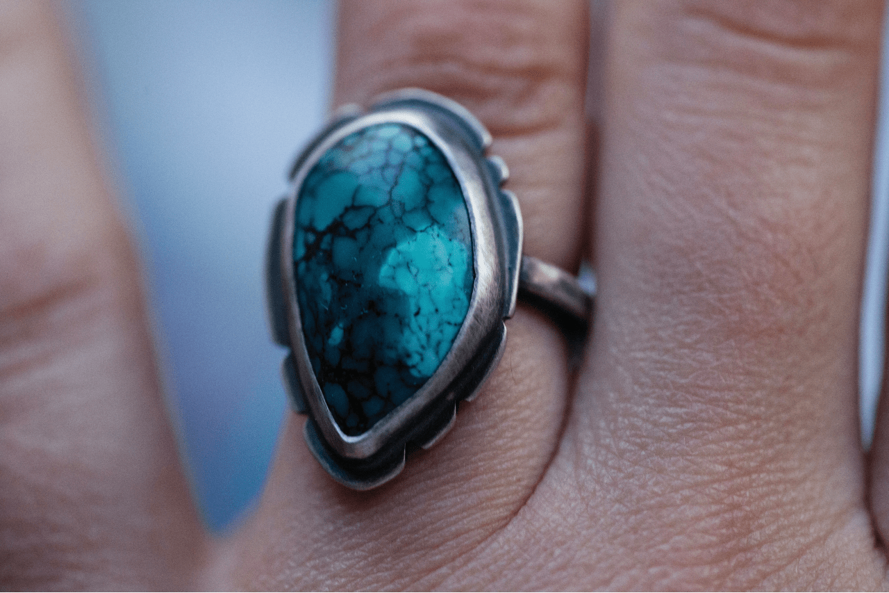 a white gold ring featuring a large turquoise stone on a person’s third finger a white gold ring featuring a large turquoise stone on a person’s third finger