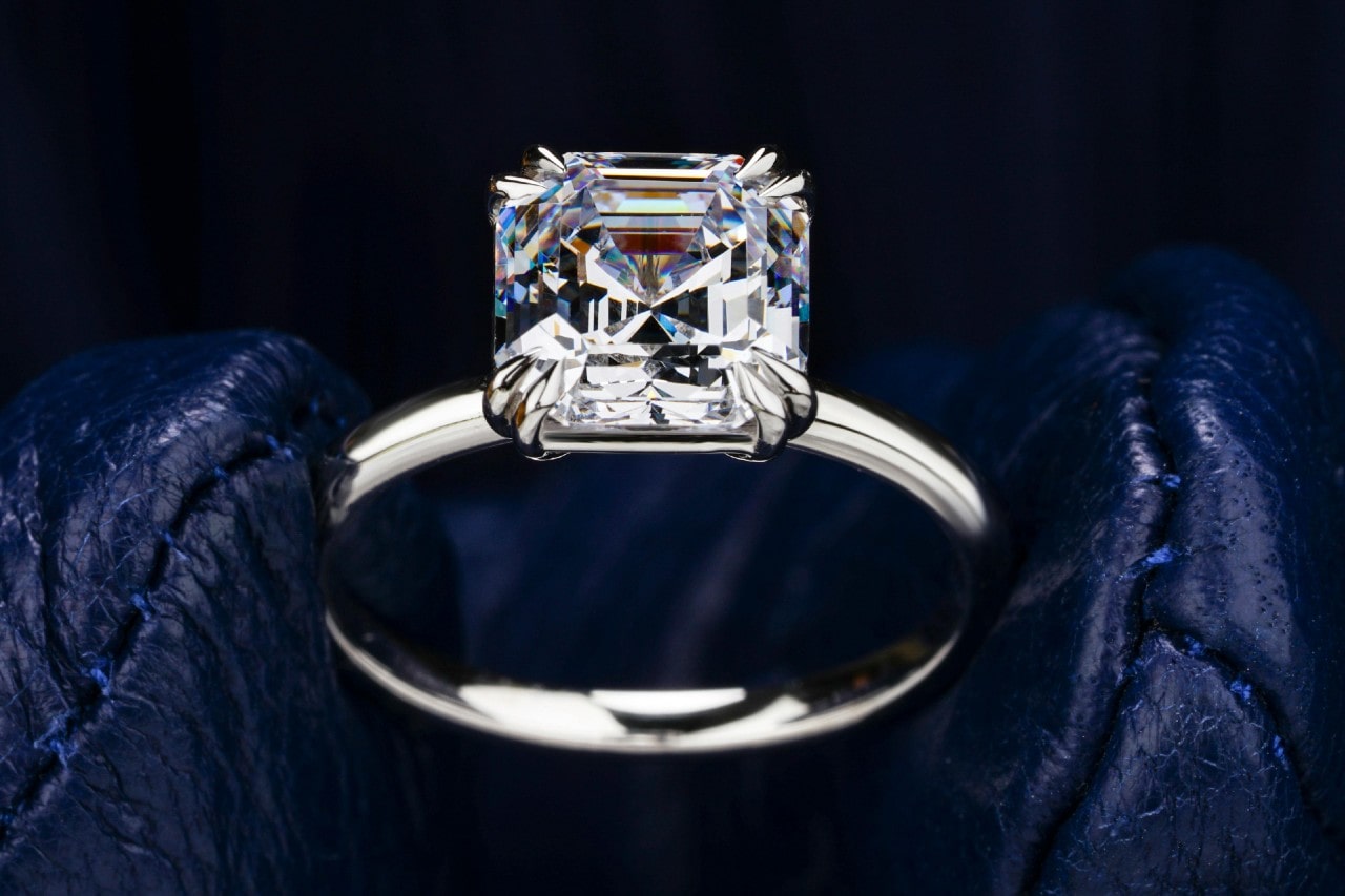 a white gold engagement ring with an asscher cut center stone held by gloved fingers a white gold engagement ring with an asscher cut center stone held by gloved fingers