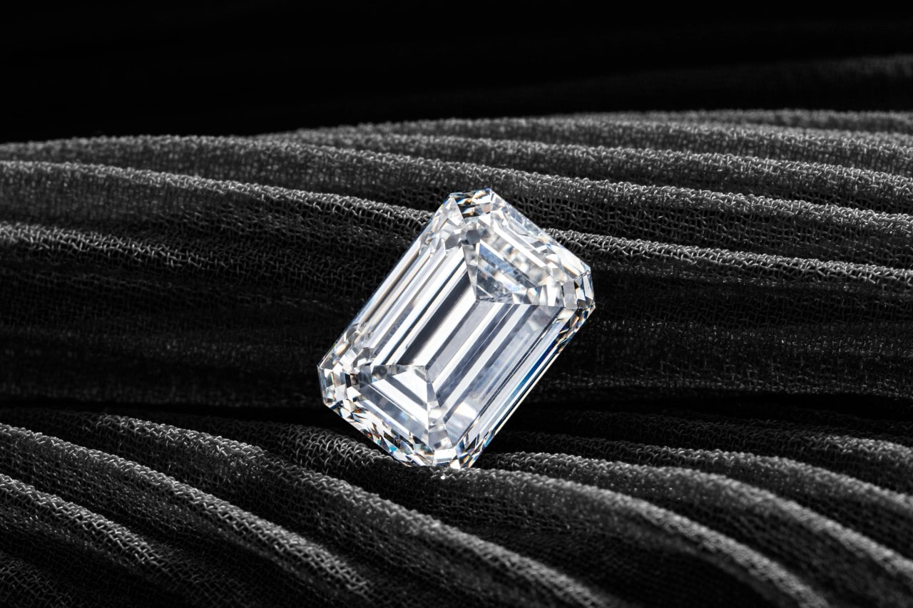 A close up of an emerald cut diamond on a dark textured fabric