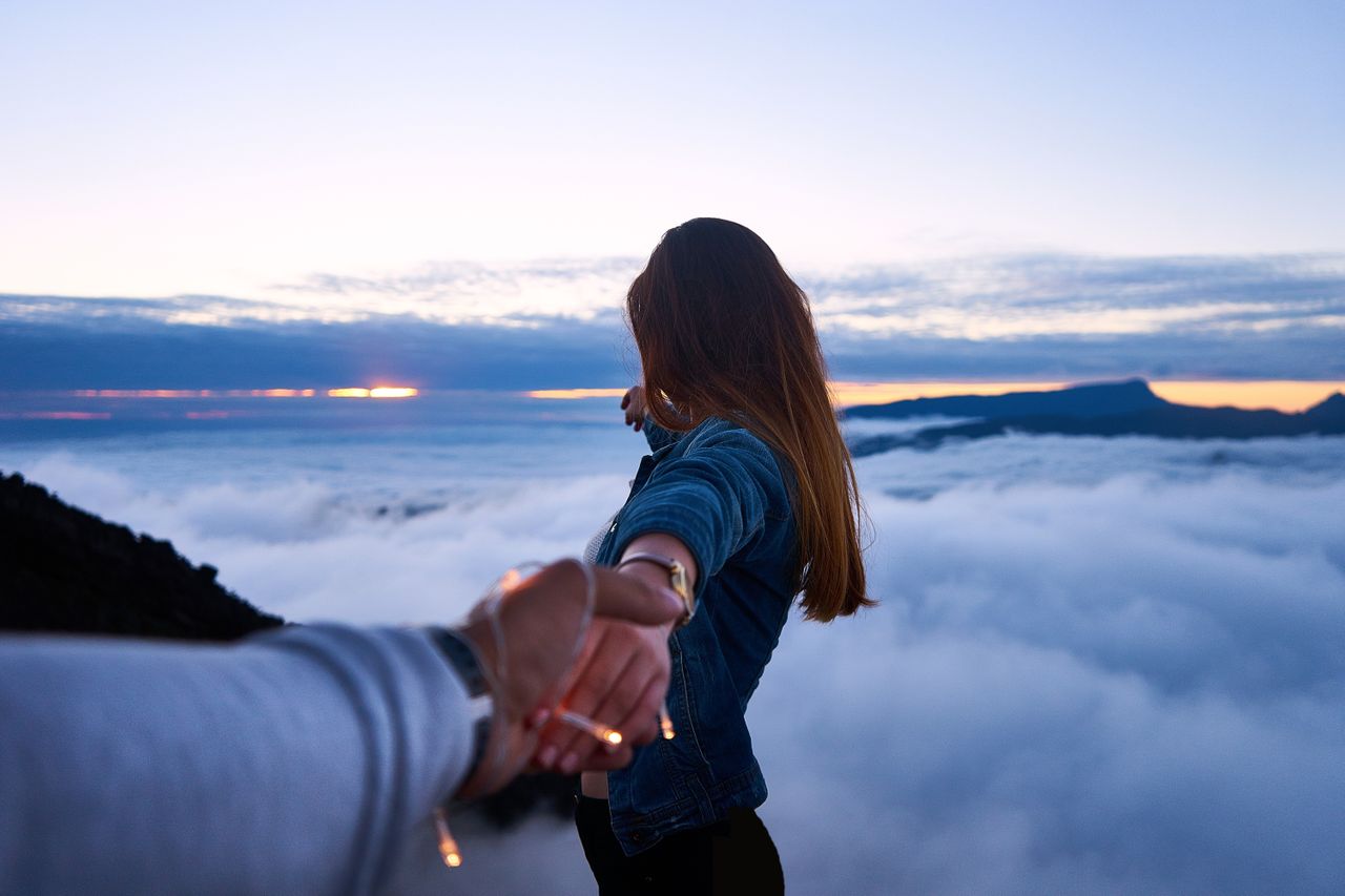 A couple holds hands, the woman stretches out to touch the horizon.