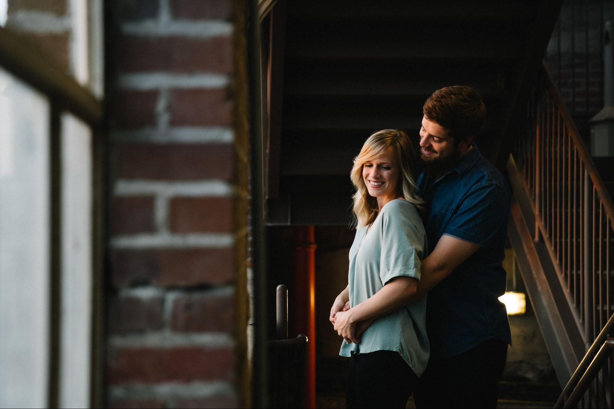 A couple embraces downstairs as they look through a window in the morning.