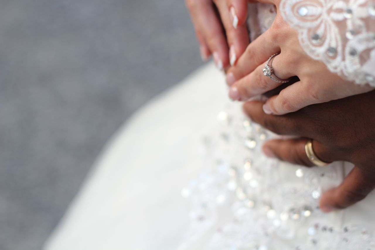 A bride and groom embracing, a close up of their hands wearing wedding rings.