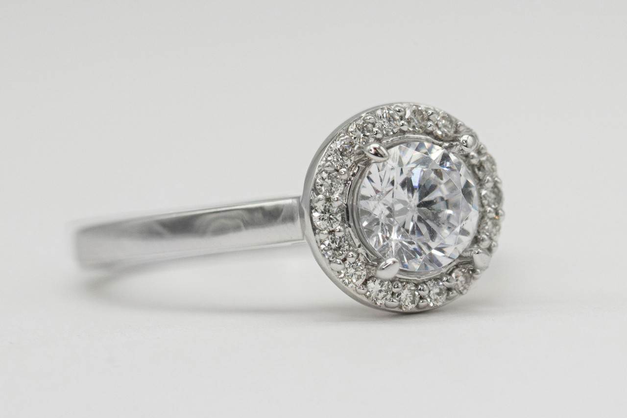 A white gold halo engagement ring with a large round brilliant-cut centre diamond surrounded by a circle of smaller diamonds. A white gold halo engagement ring with a large round brilliant-cut centre diamond surrounded by a circle of smaller diamonds.
