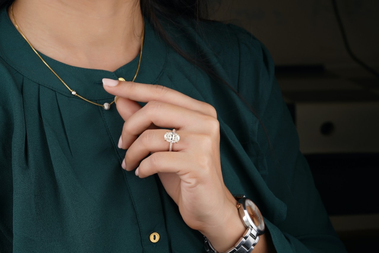 a woman in a green top wearing an engagement ring with a large, oval cut center stone