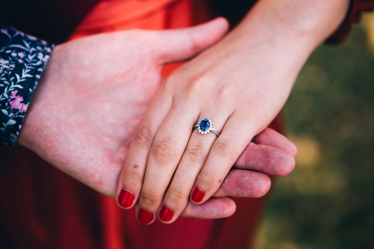 A man’s hand holding a woman’s, the woman wearing a sapphire engagement ring. A man’s hand holding a woman’s, the woman wearing a sapphire engagement ring.